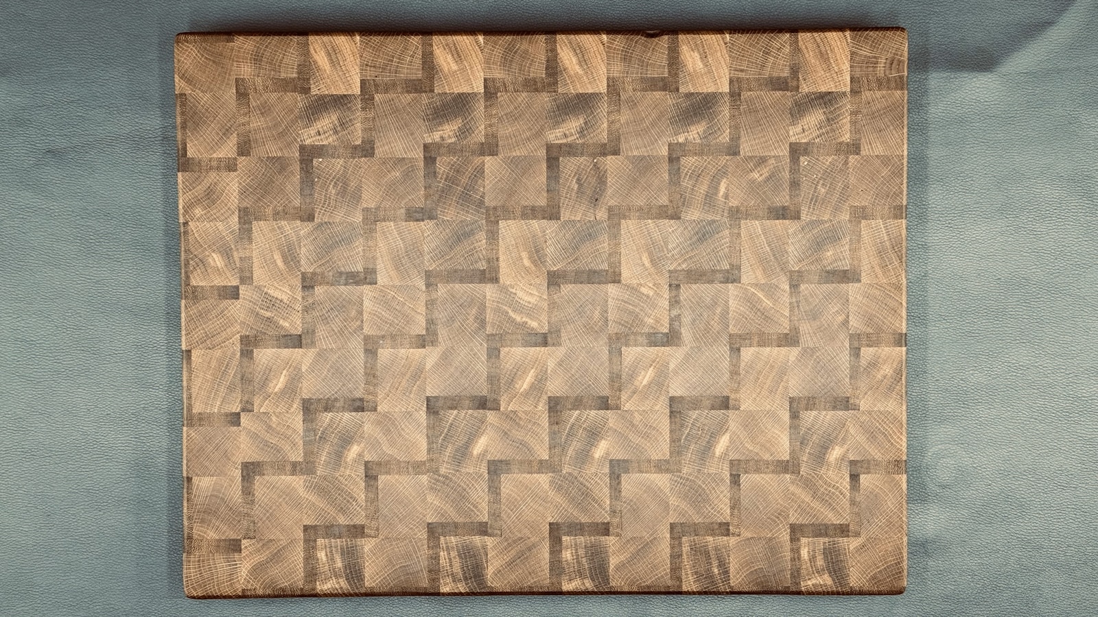 End-grain cutting board with a geometric woven wood pattern on a clean light surface