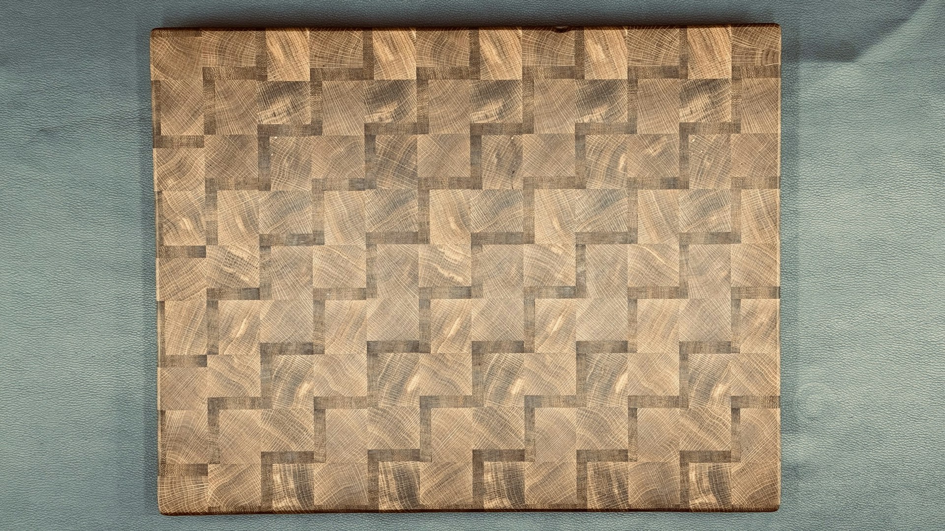 Close-up of a woven-pattern end-grain cutting board showing alternating wood grain blocks in warm and dark tones