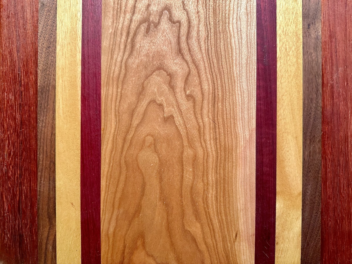End-grain cutting board with vivid contrasting wood strips in purple, orange-red, and light tan