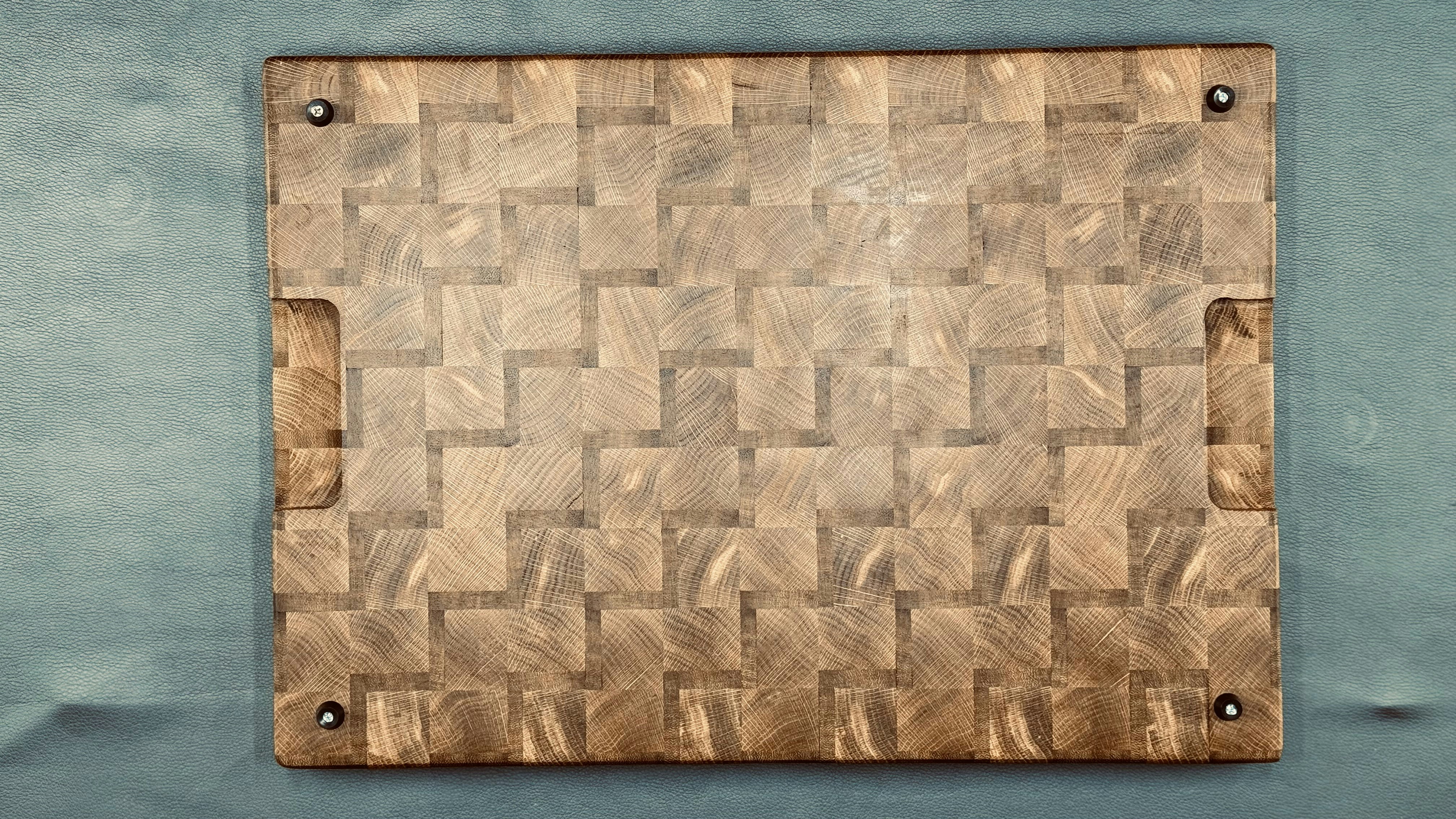 Handcrafted end-grain cutting board with a parquet block pattern and visible wood grain rings, set against a soft teal background