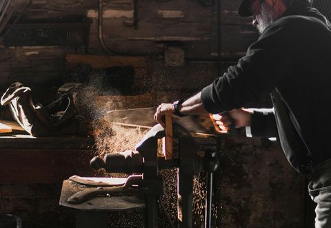 Craftsman cutting wood with a hand saw in a dimly lit workshop