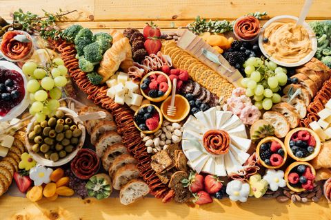 An overhead view of a charcuterie board spread with cured meats, cheeses, grapes, and crackers arranged on a wooden board