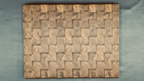 Close-up of a woven-pattern end-grain cutting board showing alternating wood grain blocks in warm and dark tones