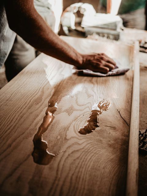 Person applying oil finish to a wooden surface with a cloth, rubbing it into the grain