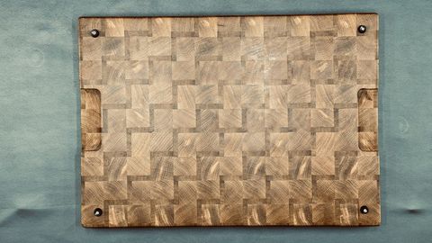 Handcrafted end-grain cutting board with a parquet block pattern and visible wood grain rings, set against a soft teal background